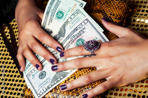 pretty fingers of african american woman holding money closeup with purse, luxury jewellery on python clutch, cash for gifts