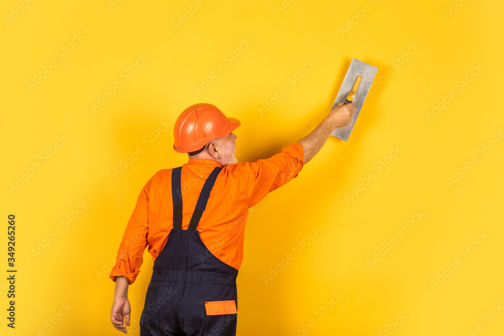 plaster trowel spatula on yellow drywall plasterboard. Plasterer in working uniform plastering wall indoor. man with spatula. process of applying layer of putty. Plastering tools for plaster plaster trowel spatula on yellow drywall plasterboard. Plasterer in working uniform plastering wall indoor. man with spatula. process of applying layer of putty. Plastering tools for plaster