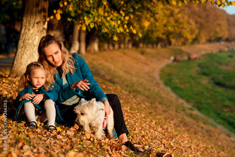 Fototapeta premium Mother and little child playing with a dog among autumn leaves. Family vacation.