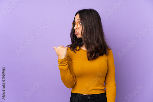 Young mixed race woman isolated on purple background unhappy and pointing to the side