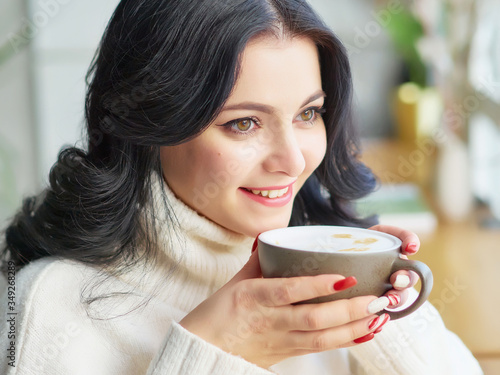 a pretty brunette girl in a white blouse is sitting in a cafe and holding a Cup of coffee. smile. close up. copy space.