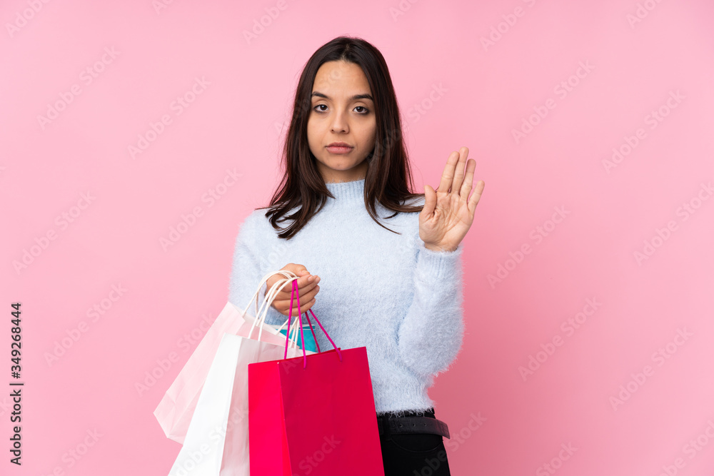 Young woman with shopping bag over isolated pink background making stop gesture