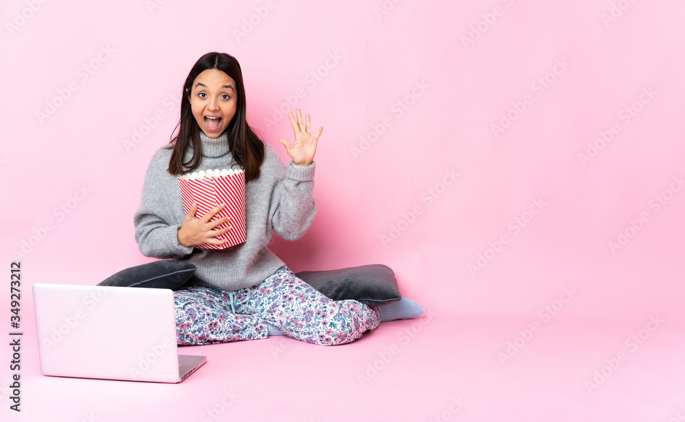 Young mixed race woman eating popcorn while watching a movie on the laptop counting five with fingers Young mixed race woman eating popcorn while watching a movie on the laptop counting five with fingers