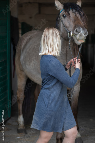 Beautiful young girl next to a horse in the stable against a dark background.