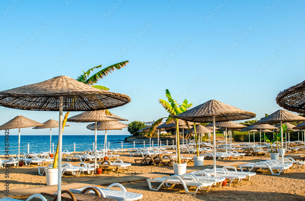 Empty sandy beach at hotel without tourists. Loose white plastic sunbeds. calm blue sea. Summer holiday on coast concept. Vacation background. Holiday backdrop.