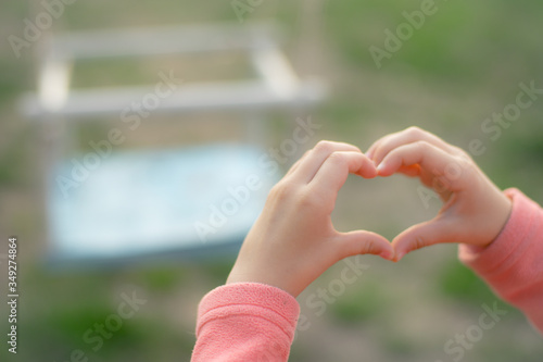 heart made of fingers, hands of a little girl on a playground, swing in blured background