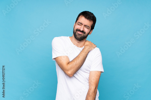 Young man with beard over isolated blue background suffering from pain in shoulder for having made an effort