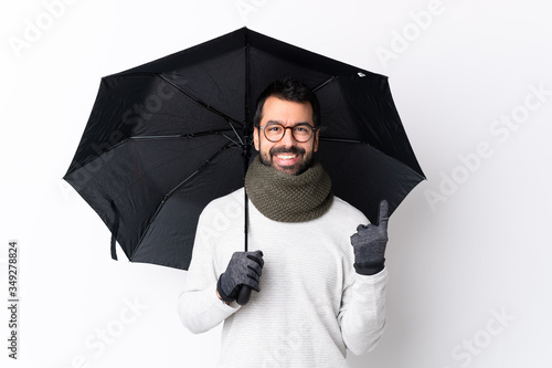 Caucasian handsome man with beard holding an umbrella over isolated white wall pointing up a great idea photo