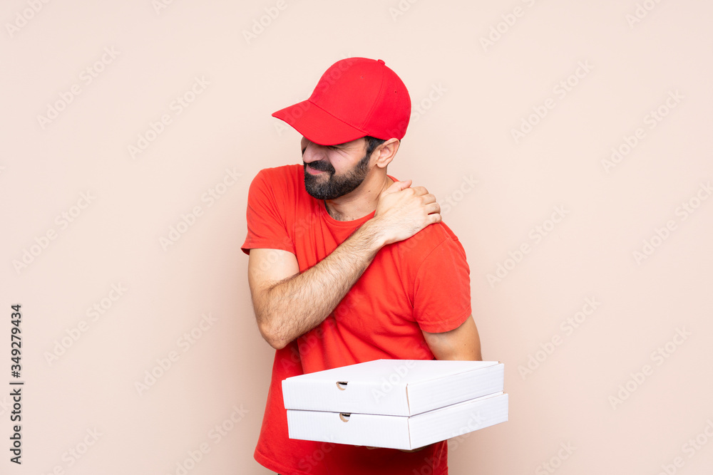 Young man holding a pizza over isolated background suffering from pain in shoulder for having made an effort Young man holding a pizza over isolated background suffering from pain in shoulder for having made an effort