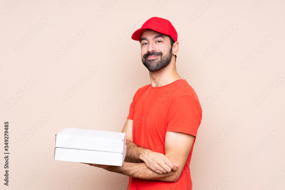 Young man holding a pizza over isolated background with arms crossed and looking forward Young man holding a pizza over isolated background with arms crossed and looking forward