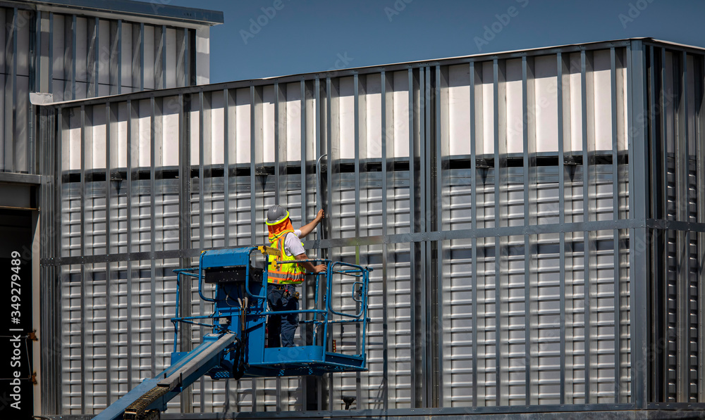Construction worker on blue man lift working on metal prefab building with grid pattern