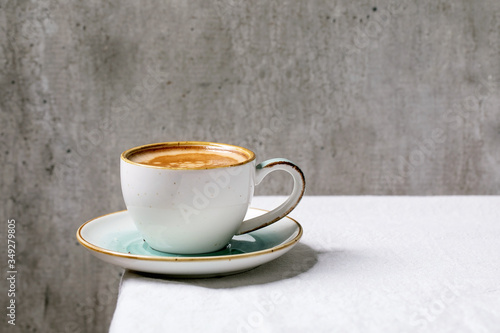 Black coffee espresso with foam in white ceramic cup with saucer standing on white cotton table cloth. Copy space