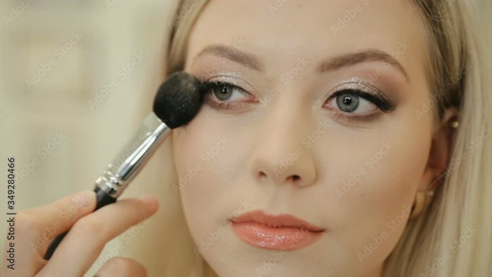 Makeup artist applying blush to cheek of woman. Professional make up artist using brush to paint cheeks of luxurious models face. Make up studio beauty salon Makeup artist applying blush to cheek of woman. Professional make up artist using brush to paint cheeks of luxurious models face. Make up studio beauty salon