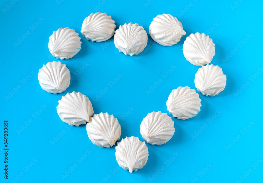 white vanilla marshmallows laid out on a blue background in the form of hearts. breakfast for a loved one. wedding concept white vanilla marshmallows laid out on a blue background in the form of hearts. breakfast for a loved one. wedding concept