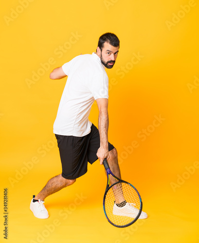 Full-length shot of man playing tennis over isolated yellow background © luismolinero