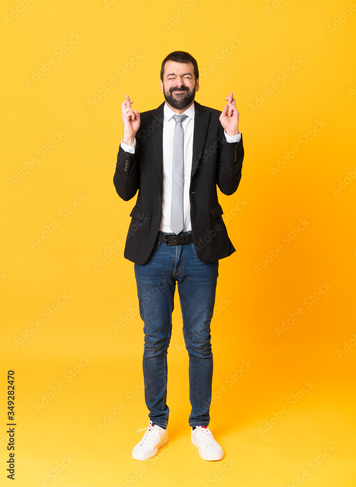Full-length shot of business man over isolated yellow background with fingers crossing and wishing the best Full-length shot of business man over isolated yellow background with fingers crossing and wishing the best