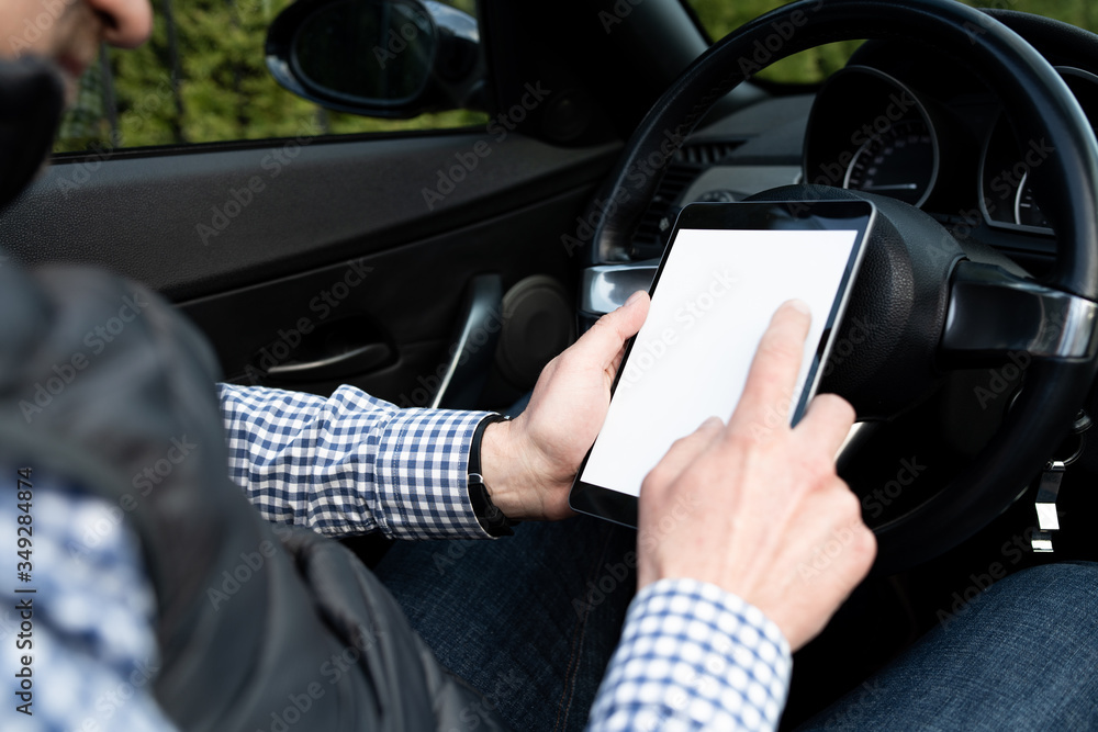 Man sitting in a car and browsing mobile device. Closeup of a young businessman using a tablet in a cabrio.