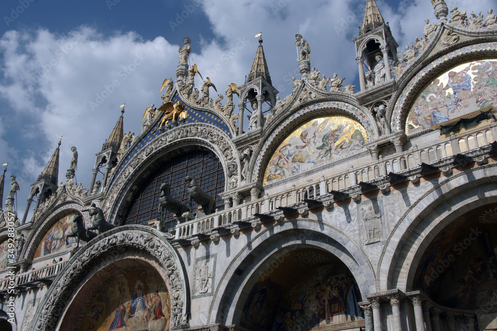 Marble facade of St. Mark's Cathedral with mosaics, sculptures in Venice in sunny summer day.