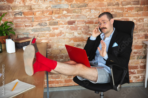 Greeting. Young man without pants but in jacket working on a computer, laptop. Remote office during coronavirus, fun and comfortable in underpants. Insulation, quarantine, humor, business concept. photo