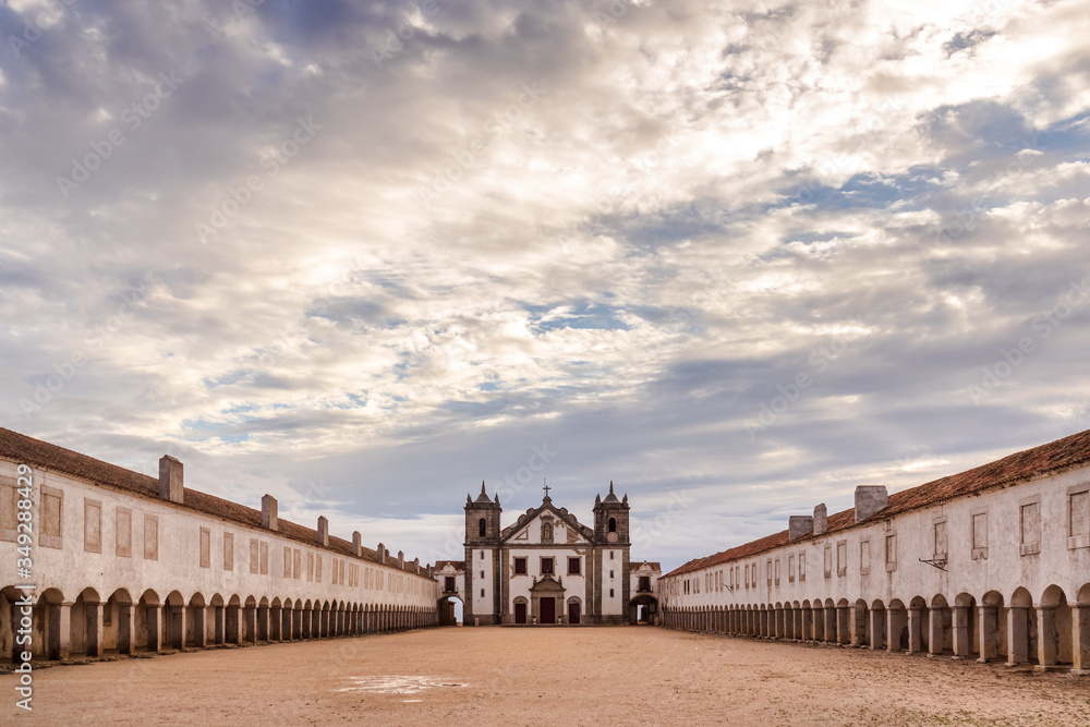 Fototapeta premium The Nossa Senhora do Cabo church, located in Espichel Cape, Sesimbra in the Setubal peninsula, with its archs leading to the main building, on a cloudy day with the sun shining through the clouds