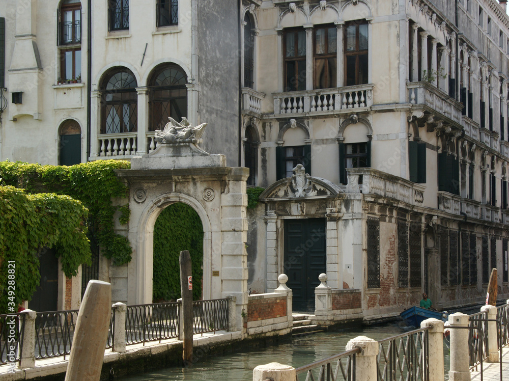 Naklejka premium Photo of canal in Venice with historical facades with balustrades, greenery, piles, boat.