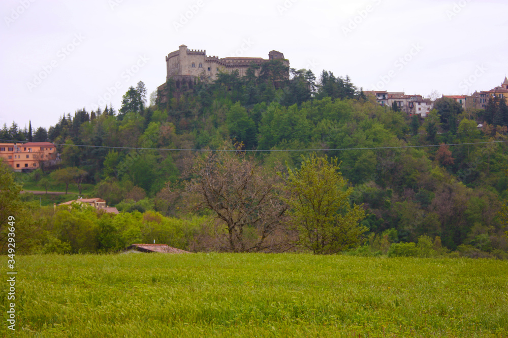 a feudal castle of the Lunigiana in the distance on the hill among the green fields on a cold day and gray sky
