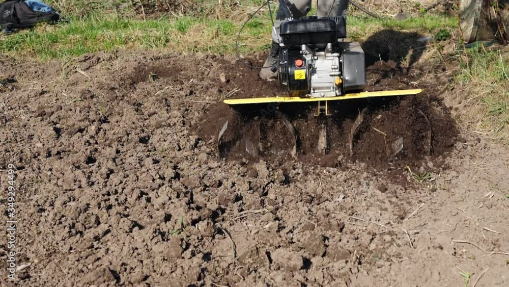 Rotary tiller blades loosen the soil, the ground scatters from cutter wheel . A farmer with a mini petrol cultivator plows a field,slow motion.