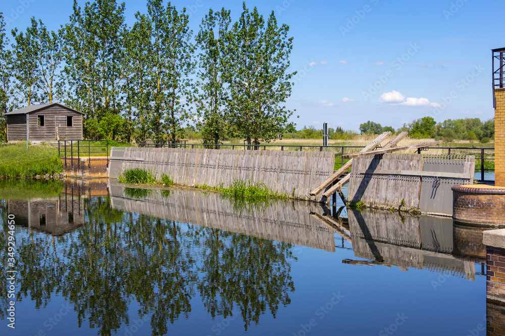 View of an historical weir system. In the background there is a row of poplars.