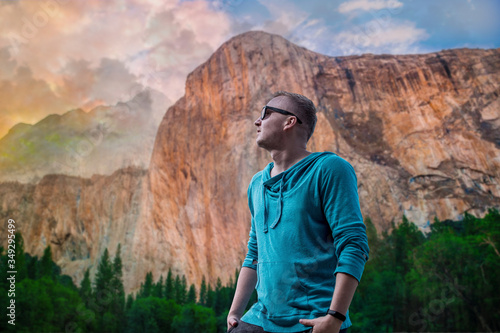 young man with a sunglass standing and looking on a huge rock. Shocked young boy traveler in stylish clothes is looking on mountains and clouds. space for text