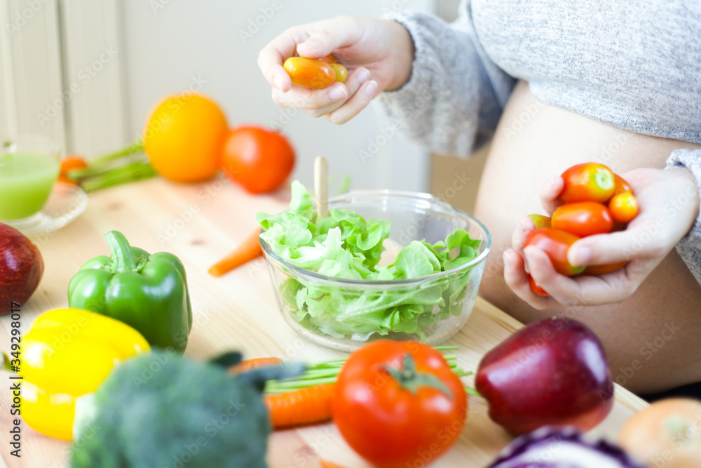 Pregnant women wear long sleeved gray sweaters. She is holding tomatoes and is preparing a salad to put on a glass cup on the cooking table. The table is full of fresh vegetables. Mummy nutrition Pregnant women wear long sleeved gray sweaters. She is holding tomatoes and is preparing a salad to put on a glass cup on the cooking table. The table is full of fresh vegetables. Mummy nutrition