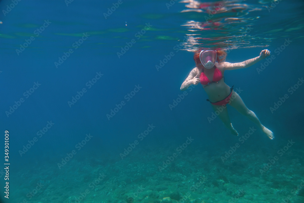 Woman in a full-face mask for snorkeling on distance. Under the water. dives to the bottom. having fun at sea. vacation and rest at sea. bright colours. Copy space