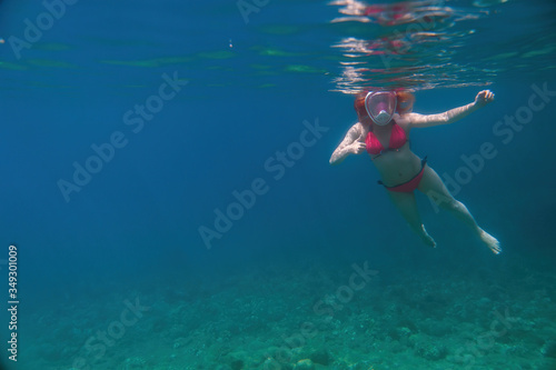 Woman in a full-face mask for snorkeling on distance. Under the water. dives to the bottom. having fun at sea. vacation and rest at sea. bright colours. Copy space