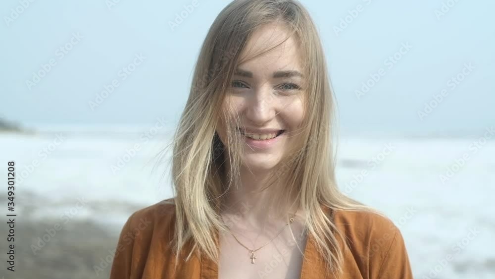 Portrait of a young happy girl traveler with developing hair in the wind on the background of a spring sea beach with snow. looks at the camera and laughs. relaxation and freedom in nature Portrait of a young happy girl traveler with developing hair in the wind on the background of a spring sea beach with snow. looks at the camera and laughs. relaxation and freedom in nature