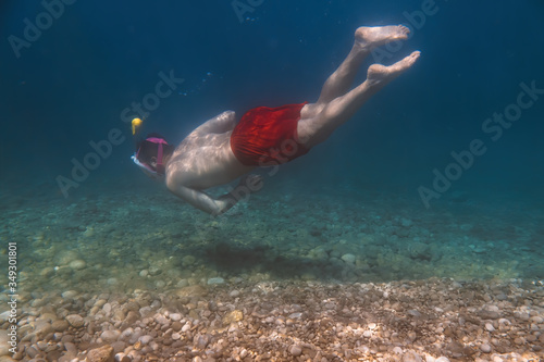 Snorkeler, snorkeling man in full face mask, summer vacation activity, swimming in the warm tropical sea, seashore and fishes, starfishes near rocks, Italy
