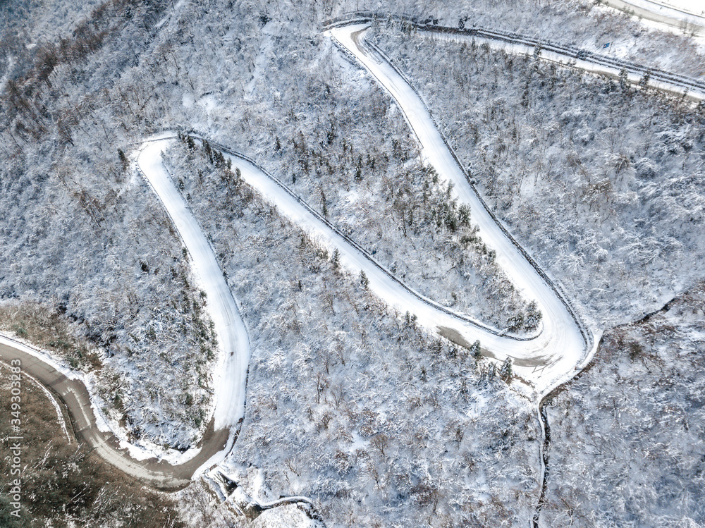 Aerial view of the curved mountain roads going up the hill through the pine and other trees covered with snow in winter. Mountains in Sichuan in Xiling.