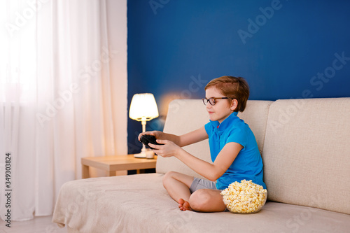 Leisure time, children, technology and people concept - little blonde boy with gamepad playing video game at home