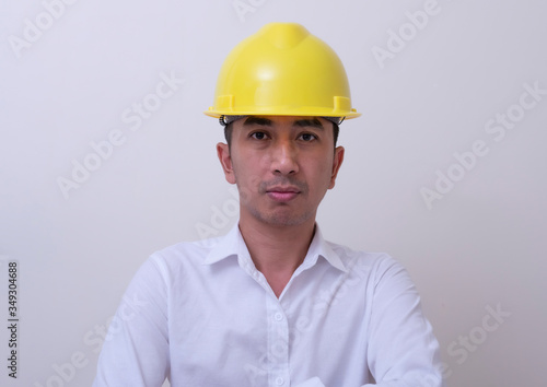 engineer with hands crossed wearing yellow helmet on white background
