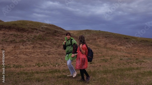 free female travelers go to gorge  holding hands. teamwork travelers. Healthy tourist girls travel with backpacks in colorful raincoats  storm is approaching. concept of adventure and travel.