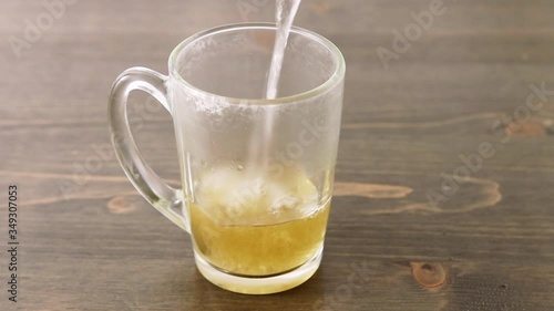 Pour hot water onto a herbal medicine tablet in an empty glass on a wooden table. Stirring with teaspoon. Bubbles, steam and splashes. Concept for self-medication and natural medicine