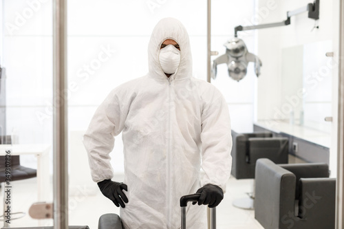tecnico con respiratore protettivo e tuta bianca pronto per la sanificazione antivirus e antibatterica  in salone di parrucchieri  .