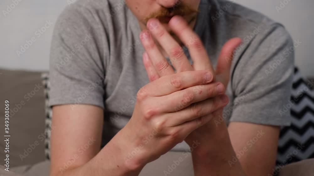 Tired young man sitting on bed massaging hand suffering from rheumatoid