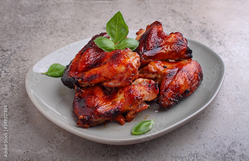 Grilled chicken wings in soy sauce decorated with basil in a plate on a concrete background