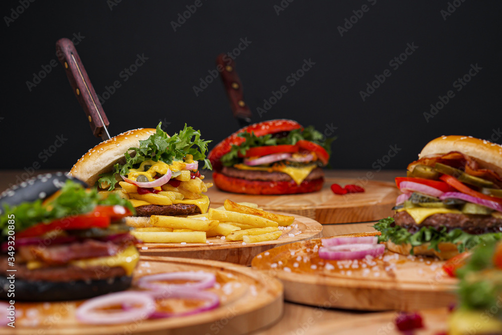 Fototapeta premium A set of different burgers. Fast food restaurant board. A diverse snack menu. Serving on a wooden board on a black background.