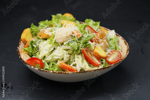 Caesar salad with shrimp in a bowl on a black background.