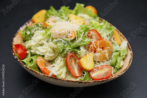 Caesar salad with shrimp in a bowl on a black background.