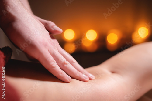 Close-up low key on woman's thigh massage in a professional premium spa salon, man masseur does in a dark room on the background of burning candles