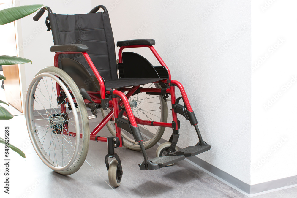Nursing crisis concept. Wheelchair at home in anteroom and part of rubber plant on grey floor