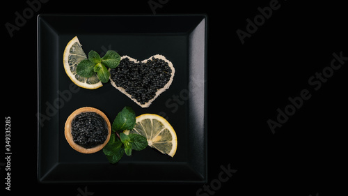 Tartlets and sandwiches with black sturgeon caviar on plate with fresh lemon, ice cube, mint. Healthy diet. Selective focus Copy space Space for text