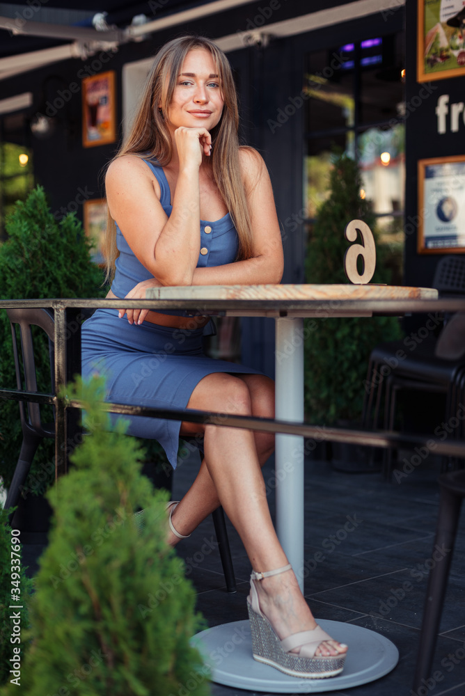 Vertical photo of a girl in a cafe. A girl in a blue top sits sideways. Vertical photo of a girl in a cafe. A girl in a blue top sits sideways.