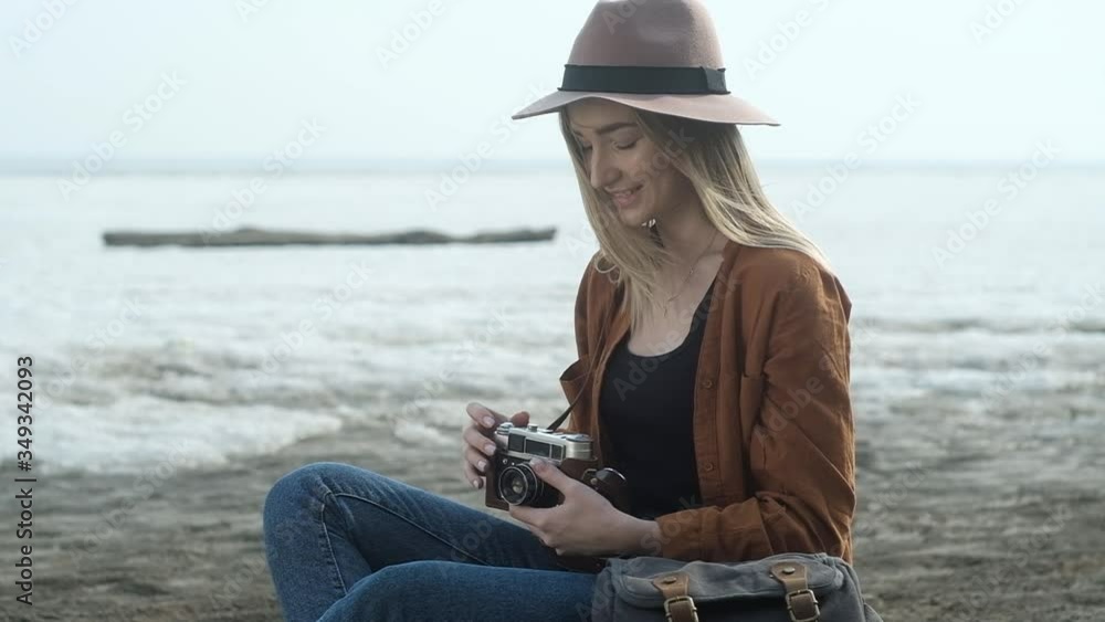 Stylish girl sitting on the sand near the frozen sea. A woman uses an old retro camera and takes beautiful pictures of the landscape. happy girl travels and takes pictures on camera Stylish girl sitting on the sand near the frozen sea. A woman uses an old retro camera and takes beautiful pictures of the landscape. happy girl travels and takes pictures on camera
